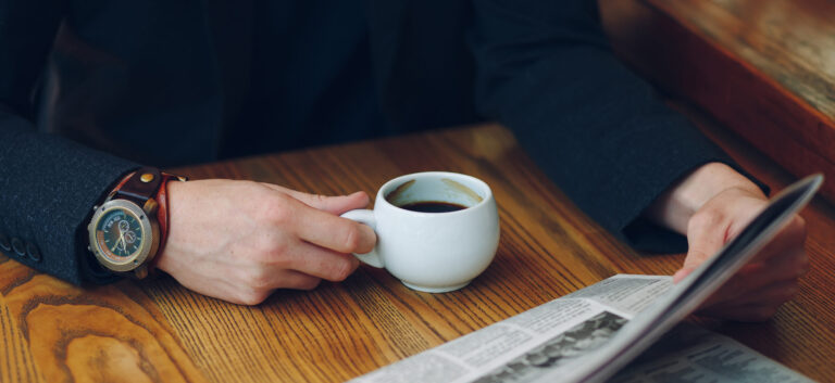 Man's hands close-up holding cup of coffee and a newspaper